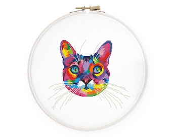 Könnte beinhalten: Ein farbenfrohes Kreuzstichmuster eines Katzenkopfes mit leuchtenden Farben wie Rot, Gelb, Blau und Lila. Die Augen der Katze sind blau, die Schnurrhaare weiß. Das Kunstwerk befindet sich in einem runden Stickrahmen.