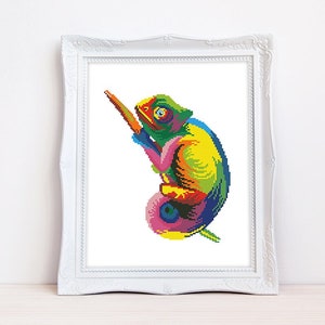 以下が含まれることがあります： 虹色のカラーパレットで描かれた、カラフルなカメレオンのクロスステッチパターン。カメレオンは枝に止まっており、舌を伸ばしています。