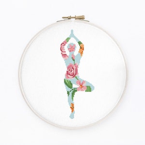 May include: Cross stitch pattern of a person in a yoga pose, with floral details in shades of pink, green, and blue.