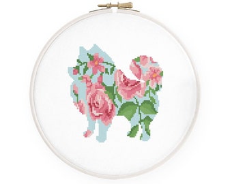 May include: A cross-stitch pattern of a white dog silhouette filled with pink roses and green leaves on a light blue background.