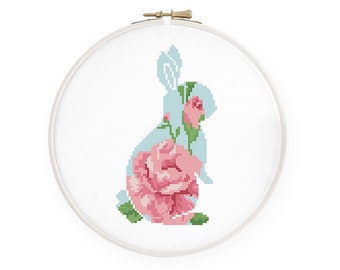 May include: A light blue bunny silhouette with a pink rose design. The bunny is surrounded by green leaves and a pink rose.