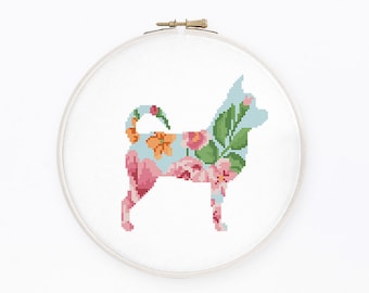 May include: A cross-stitch pattern of a chihuahua dog silhouette filled with floral designs in shades of pink, orange, and green on a light blue background. The pattern is displayed in a white embroidery hoop.