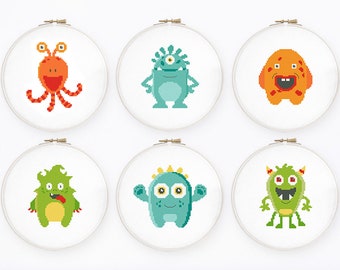 Peut inclure: Six broderies de monstres dans des cerceaux à broder. Chaque monstre est d'une couleur différente, notamment orange, vert et bleu, avec des caractéristiques pixélisées uniques. Les cerceaux sont blancs avec un fermoir doré.