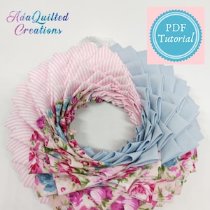 Könnte beinhalten: Ein Kranz aus Stoff in Rosa- und Blautönen. Der Kranz besteht aus mehreren Stofflagen, jede mit einem anderen Muster. Der Stoff ist gefaltet und übereinander gelegt, um einen gekräuselten Effekt zu erzielen. Der Kranz ist mit einem Blumenmuster verziert. Der Kranz ist ein DIY-Projekt und das Bild enthält den Text "PDF-Tutorial".