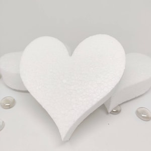 May include: Three white foam heart shapes, two are smaller and one is larger. The larger heart is in the center of the image and the two smaller hearts are on either side of it.