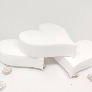 May include: Three white foam heart shapes stacked on top of each other. The hearts are smooth and have a slightly rounded edge.