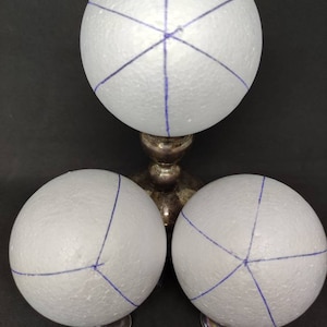 Op de afbeelding: Drie witte schuimbollen met blauwe lijnen, één op een zilveren kandelaar en twee op kleinere zilveren standaards. De bollen zijn geplaatst tegen een donkere achtergrond. De tekst "Ada Quilted Creations" staat onderaan.