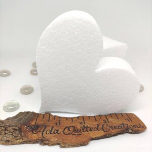 May include: A white foam heart shape measuring approximately 4 inches in length. The heart is sitting on a piece of wood with a ruler and the text "Ada Quilted Creations".