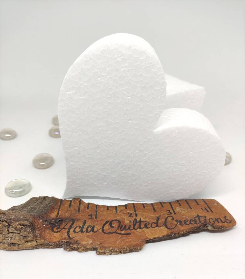 May include: A white foam heart shape measuring approximately 4 inches in length. The heart is sitting on a piece of wood with a ruler and the text "Ada Quilted Creations".