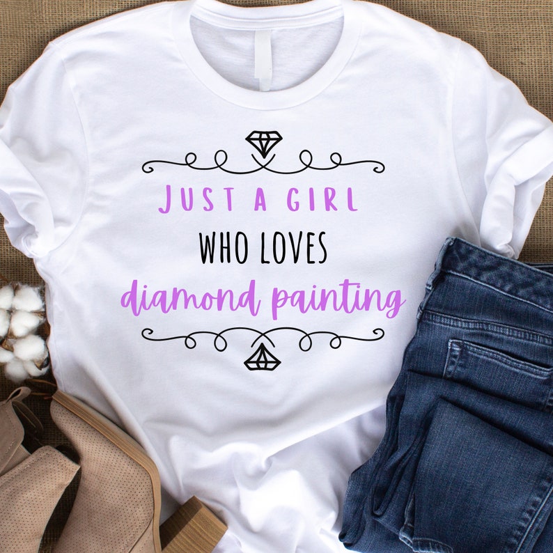 Puede incluir: Camiseta blanca con el texto "Just a girl who loves diamond painting" en letras negras y moradas. El texto est&aacute; rodeado de espirales decorativos.