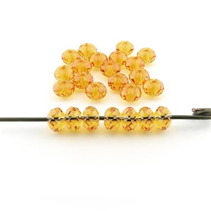May include: A strand of amber-colored faceted glass beads strung on a wire. The beads are round and have a faceted design. There are also loose beads scattered around the strand.