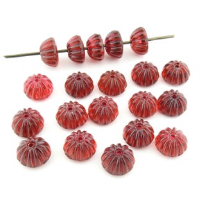 May include: A collection of 19 deep red glass beads with a fluted design. The beads are arranged in a scattered pattern on a white background.