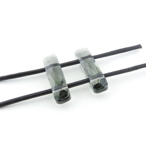 May include: Two clear faceted glass beads with a dark green tint, strung on black leather cord.