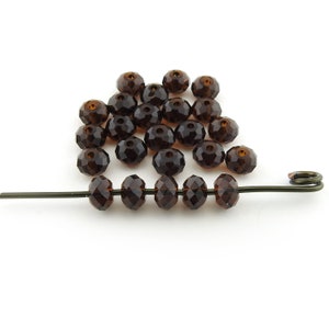 May include: A collection of faceted, dark brown beads. Some beads are loose, while others are strung on a dark wire. The beads have a symmetrical, multi-faceted design, reflecting light. The beads are a deep, rich brown color.