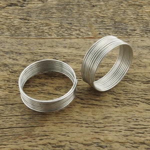 May include: Two silver wire rings, each made of multiple thin wires wrapped around each other, are lying on a wooden surface.