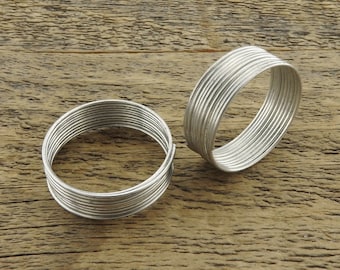 May include: Two silver wire rings, each made of multiple thin wires wrapped around each other, are lying on a wooden surface.
