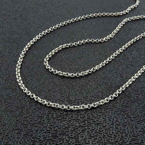 May include: A silver chain necklace with a delicate, cable chain design. The chain is shown in two lengths, laying on a black textured surface.