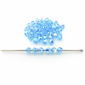 May include: A collection of light blue faceted beads, some loose and some strung on a silver-colored wire. The beads have an iridescent quality, reflecting multiple colors. The beads are likely for jewelry making or crafts.