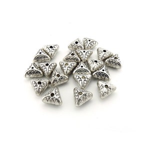 Puede incluir: Un grupo de cuentas de plata en forma de triángulo con un diseño decorativo. Las cuentas tienen un agujero en el centro para enhebrar.