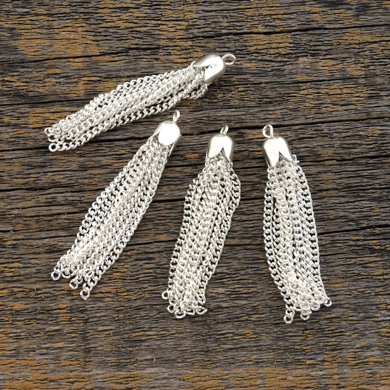 May include: Four silver chain tassels with a loop at the top for attaching to a project. The tassels are made of multiple strands of chain linked together.