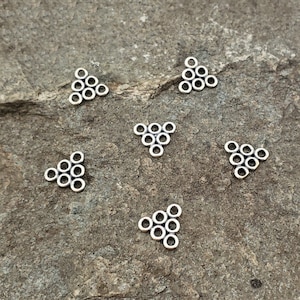 May include: Six silver triangle-shaped charms with multiple small circles forming the triangle shape.