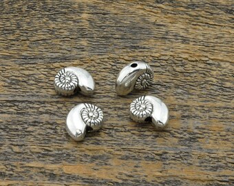 May include: Four silver-toned metal charms shaped like seashells. The charms have a detailed spiral design and a hole for threading.