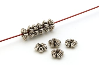 May include: Silver metal flower-shaped beads with a hole in the center. The beads are strung on a red wire.