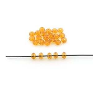 May include: A pile of amber-colored faceted glass beads, with a few beads strung on a black wire.