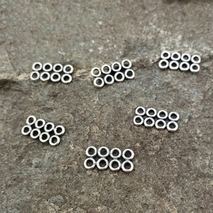 May include: Five silver metal connector pieces, each with eight small circles arranged in two rows of four. The connector pieces are on a gray textured surface.