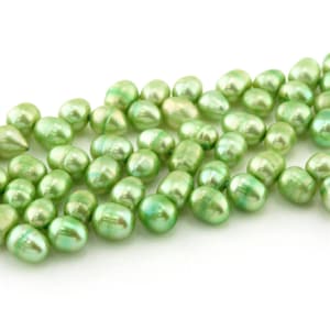 May include: A strand of green freshwater pearls. The pearls are oval shaped and have a slight iridescent sheen.