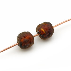 May include: Two brown glass beads with a textured surface are strung on a copper wire.
