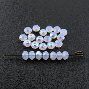 May include: A close-up of a group of iridescent, light pink, faceted glass beads. The beads are arranged in a loose circle and are strung on a thin wire.