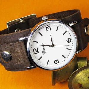 Op de afbeelding: Een bruin leren armbandhorloge met een witte wijzerplaat en zilveren wijzers. De wijzerplaat van het horloge heeft zwarte Romeinse cijfers voor de uren en zwarte minutenmarkeringen. De wijzerplaat van het horloge heeft ook het woord "Glenora" erop gedrukt.