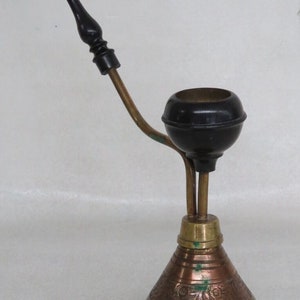 May include: A brass smoking pipe with a black wooden mouthpiece and a decorative base. The pipe has a round bowl and a long, curved stem.
