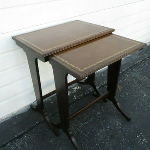 May include: A set of two brown nesting tables with a leather top and gold trim. The tables are made of wood and have a traditional design.