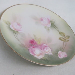 May include: A white porcelain plate with a gold rim features a delicate floral design of pink roses and green leaves.