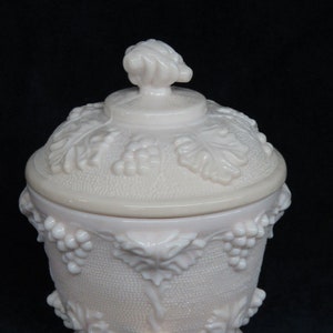 May include: A pink glass candy dish with a grapevine design and three feet. The lid has a grape cluster finial.