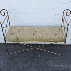 May include: A gold metal bench with a floral patterned cushion. The bench has a simple, elegant design with curved armrests.