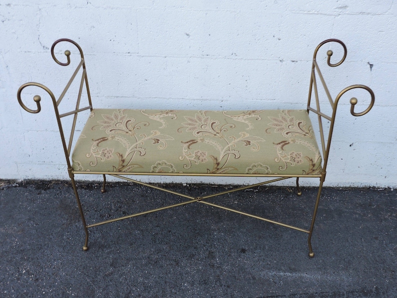 May include: A gold metal bench with a floral patterned cushion. The bench has a simple, elegant design with curved armrests.