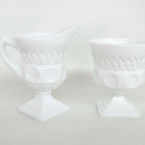 May include: A white milk glass creamer and sugar bowl set with a footed base and a diamond pattern.