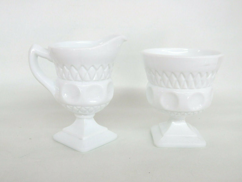 May include: A white milk glass creamer and sugar bowl set with a footed base and a diamond pattern.