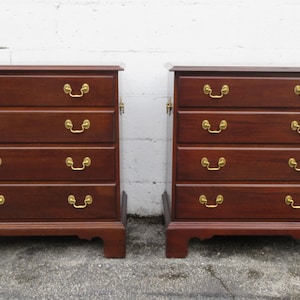 May include: Two matching wooden chests of drawers. Each chest has four drawers with brass-colored handles. The wood has a rich, dark brown finish. The chests are rectangular with a decorative base.
