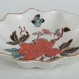 May include: A white ceramic bowl with a scalloped edge and a gold rim. The bowl features a floral design with a red peony, green leaves, and a blue butterfly.