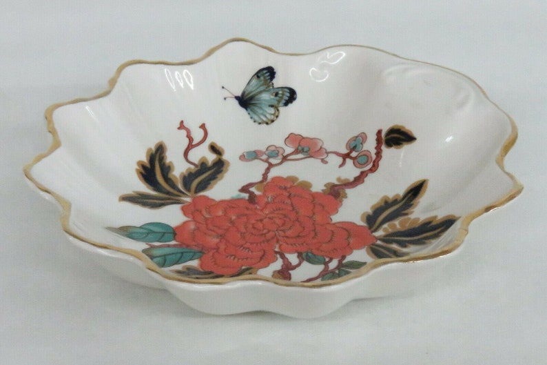 May include: A white ceramic bowl with a scalloped edge and a gold rim. The bowl features a floral design with a red peony, green leaves, and a blue butterfly.
