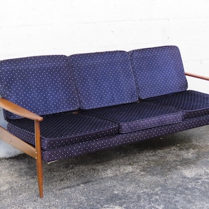May include: A three-seat sofa with a mid-century modern design. The sofa features a dark blue fabric with a white dot pattern on the cushions and backrests. The frame and armrests are made of light-colored wood.