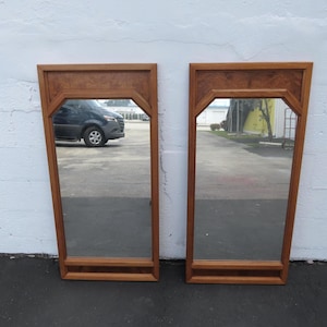 May include: A pair of rectangular wall mirrors featuring light brown wooden frames with angled upper corners and a decorative burl wood veneer panel at the top. Each mirror has a clear glass surface and a horizontal wooden bar at the base.