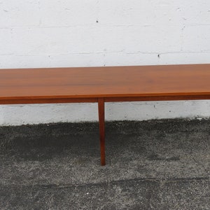 May include: A long, rectangular, wooden table with a light brown finish. The table has four legs and a simple design.
