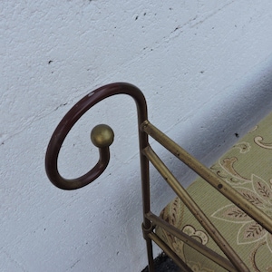 May include: A gold metal bench with a green patterned fabric cushion. The bench has a curved back with a gold ball finial.