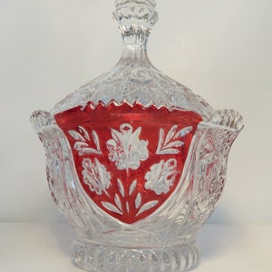 May include: A clear glass candy dish with a red and white floral design. The dish has a lid and a scalloped edge.