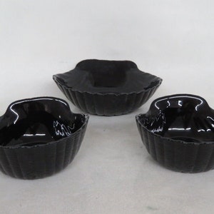 May include: Three black glass bowls with a scalloped edge. The bowls are nested together, with the largest bowl on the bottom and the smallest bowl on top.